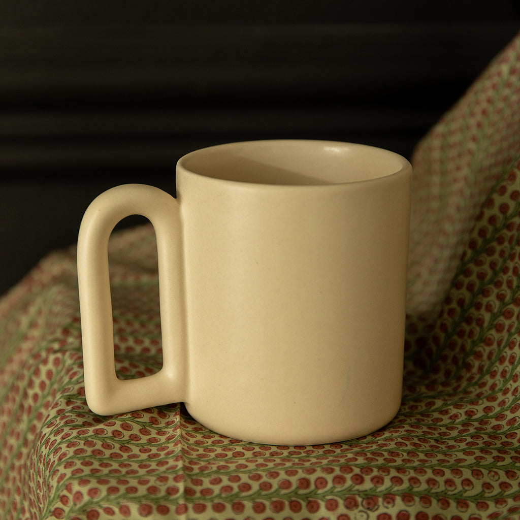 A white ceramic mug with a unique handle design, placed on a patterned fabric.