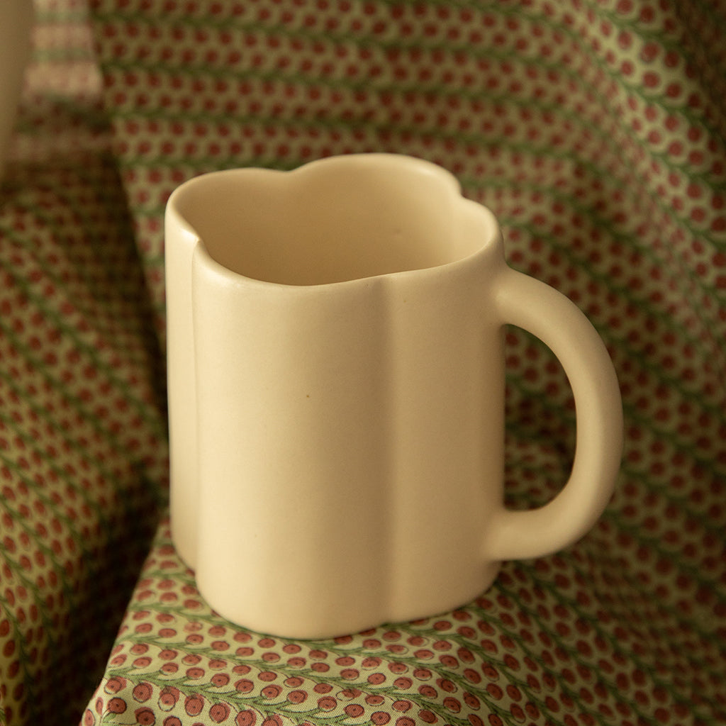 A beige ceramic mug with a subtle floral shape design, displayed on a patterned surface.