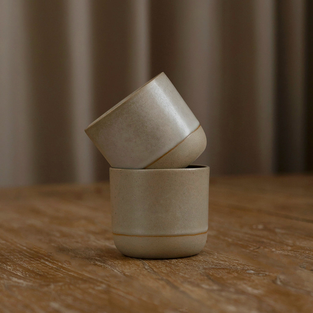 A grey ceramic cup with a modern design, placed on a wooden surface with a blurred background.