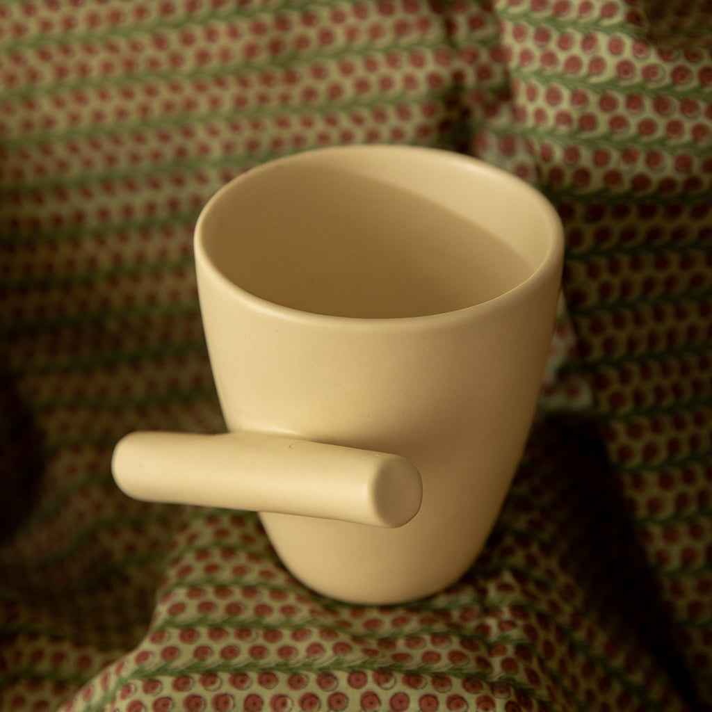 A white ceramic mug with a slanted handle, displayed on a patterned fabric.