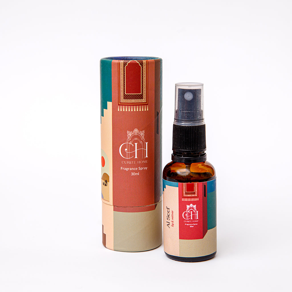 A home spray bottle of Curate Home brand with a label reading 'Al Seef' next to its cylindrical packaging tube, both featuring a colorful design.