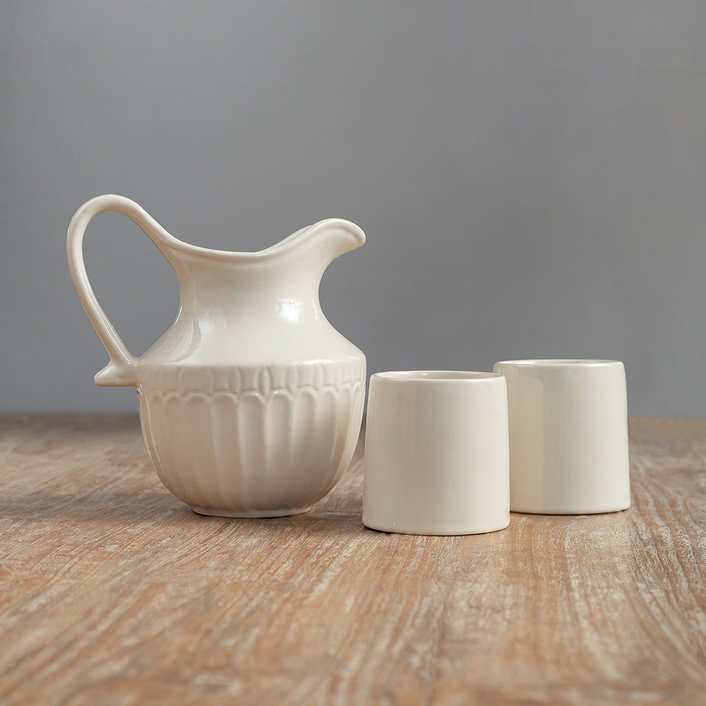 A beige ceramic jug with a vintage design of Curate Home brand accompanied by two matching ceramic glasses, placed on a wooden surface. 