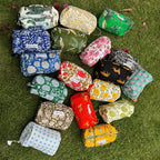A collection of hand block printed cotton pouches with various patterns, laid out on a grassy surface.