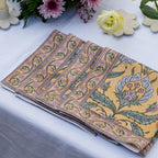 A set of folded block printed dinner napkins with a floral pattern, displayed on a table. 100% Cotton Dinner Napkins.