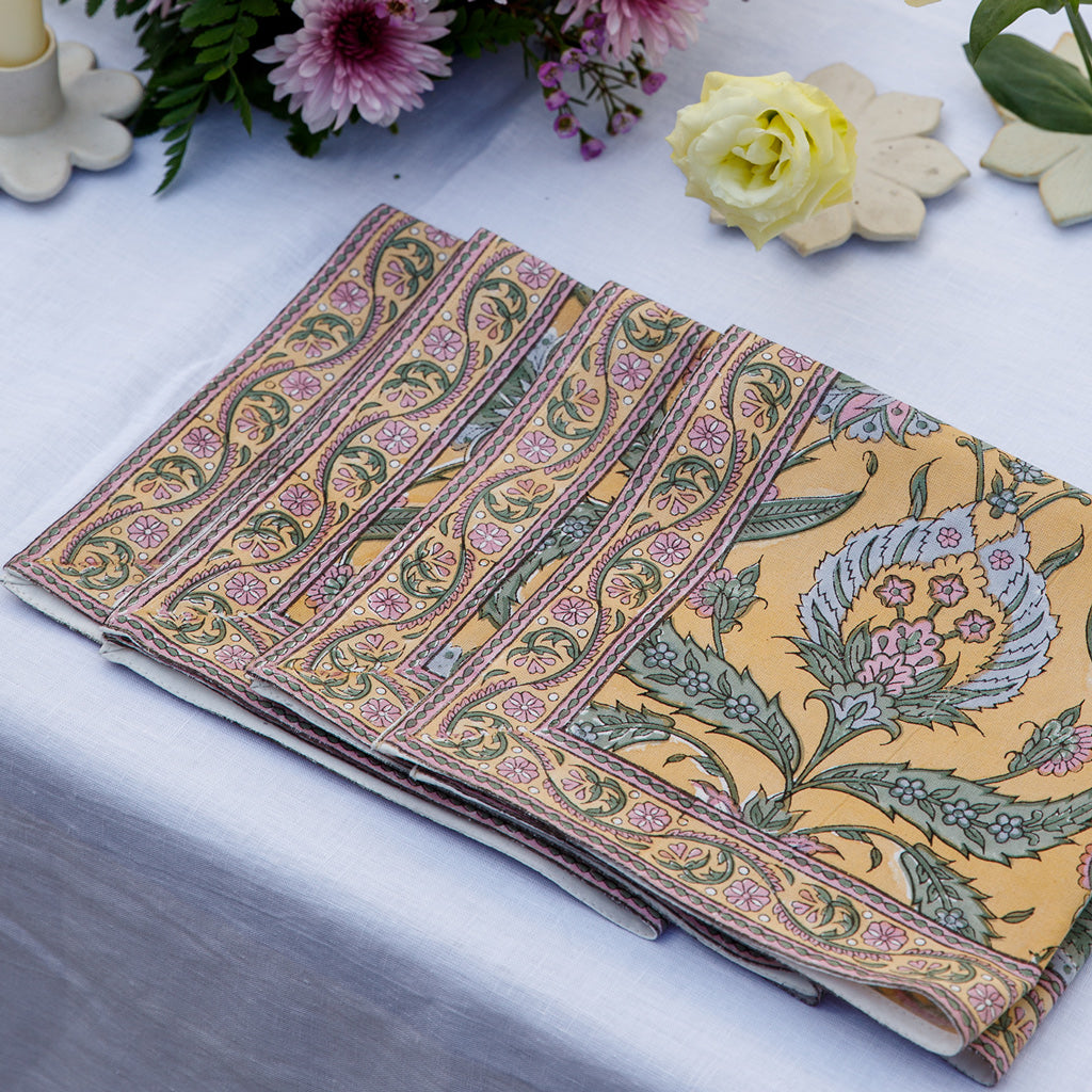 A set of folded block printed dinner napkins with a floral pattern, displayed on a table. 100% Cotton Dinner Napkins.