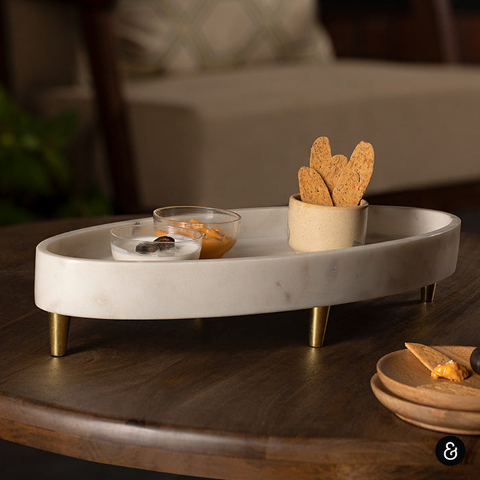 White Marble tray with snacks on a wooden table. Gondola white marble platter with brass legs.