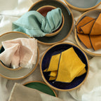 A Woven of 100% linen, these napkins have a raw fringe in various colors, including light pink and light blue.