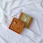 A set of four gold-colored metal napkin rings with a leaf design, displayed in an open box with a decorative pattern.