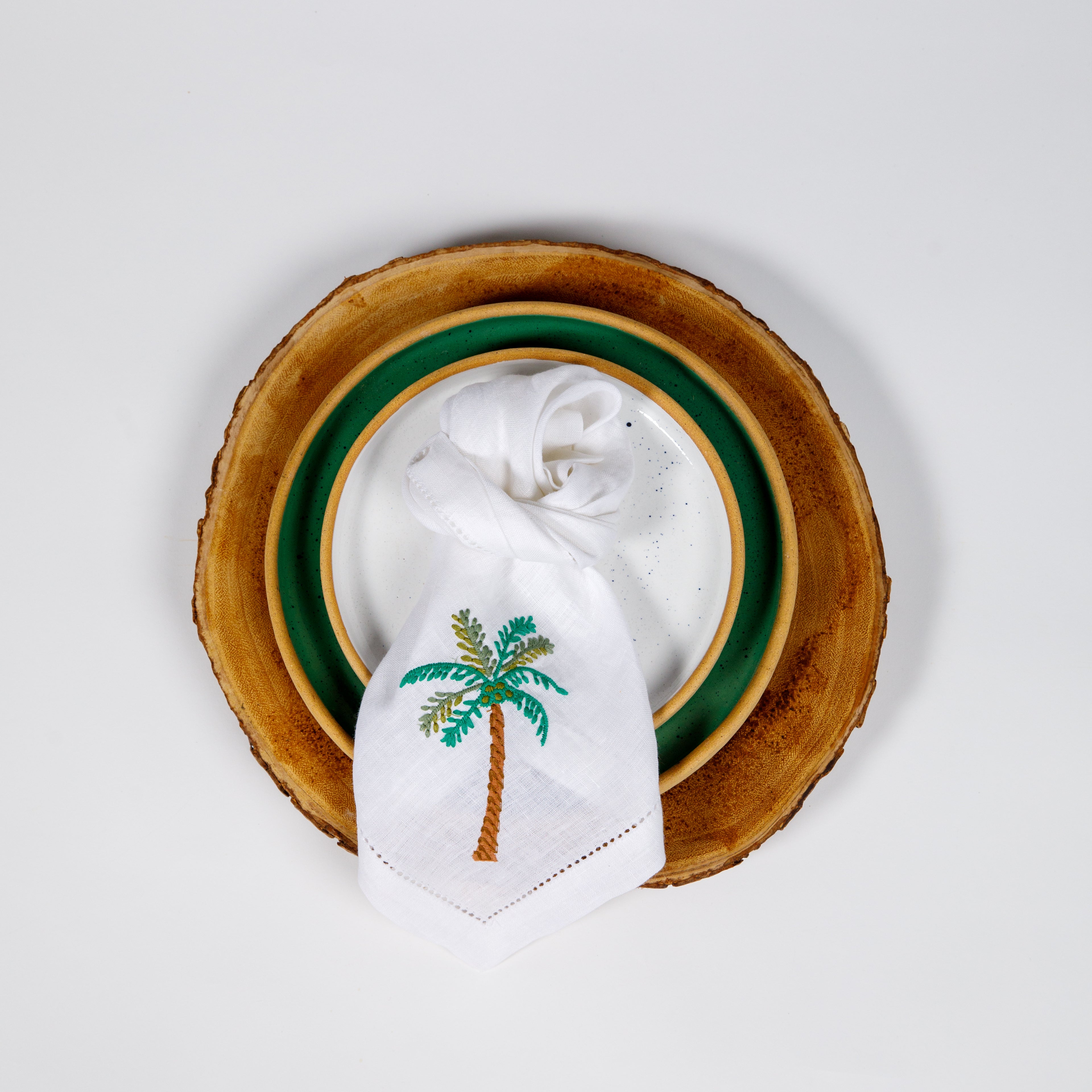 A linen napkin with a green palm tree embroidery is placed on a wooden charger plate.