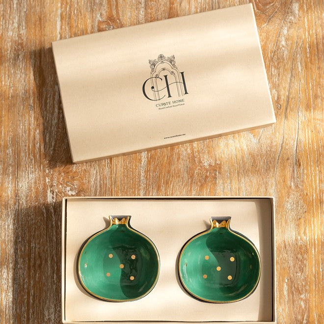 Two pomegranate shaped green ceramic bowls with gold accents in a gift box