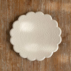 A beige, round, Ceramic stoneware serving platter with a scalloped edge, placed on a wooden surface. Diameter 30.5 cms.