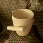 A white ceramic mug with a slanted handle, displayed on a patterned fabric.
