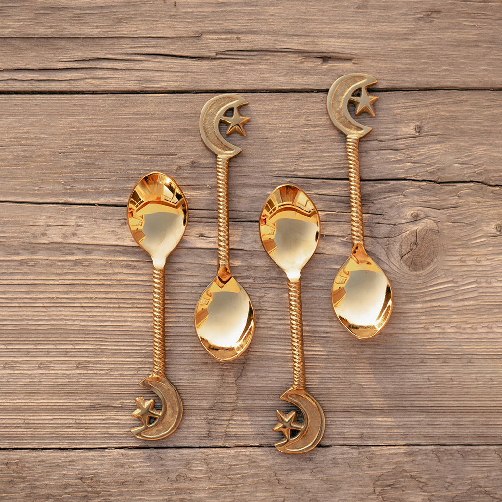 A set of four gold-colored stainless steel dessert spoons with star and moon designs on the handles, displayed on a wooden surface. length 14.6cm.