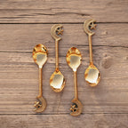 A set of four gold-colored stainless steel dessert spoons with star and moon designs on the handles, displayed on a wooden surface. length 14.6cm.