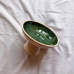 A ceramic pedestal bowl with a glossy dark green interior and a matte beige exterior