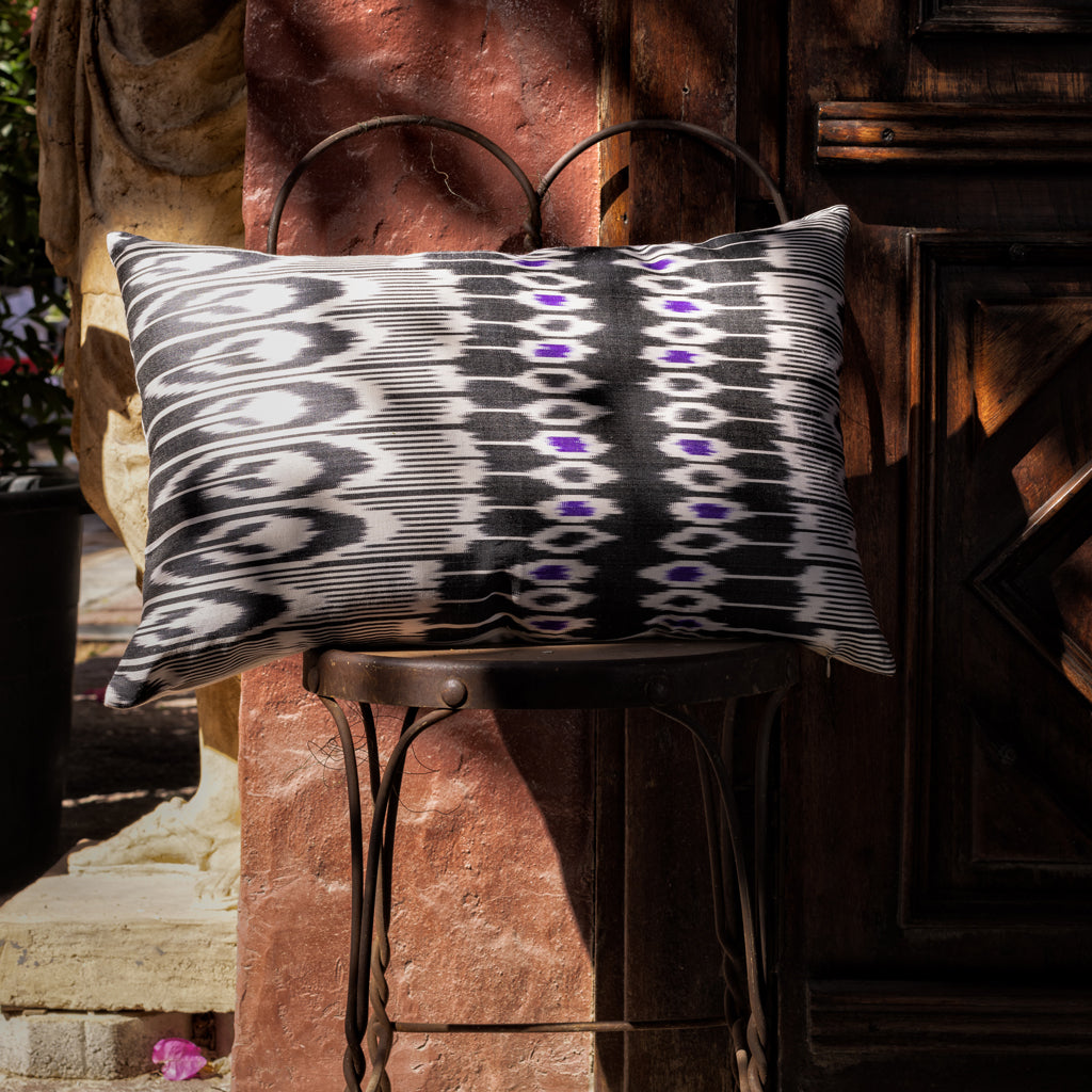 A  70% Silk 30% Cotton black and white geometric patterned ikat cushion cover displayed on a stand, with a subtle purple accent.